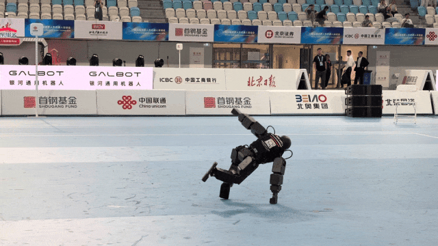 一台黑色人形机器人在体育馆地面上表演单手支撑的动态街舞定格动作。